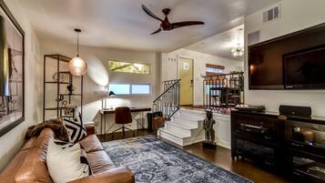 A modern living room with a leather sofa, a patterned rug, a ceiling fan, a TV, and a staircase leading to an upper level.