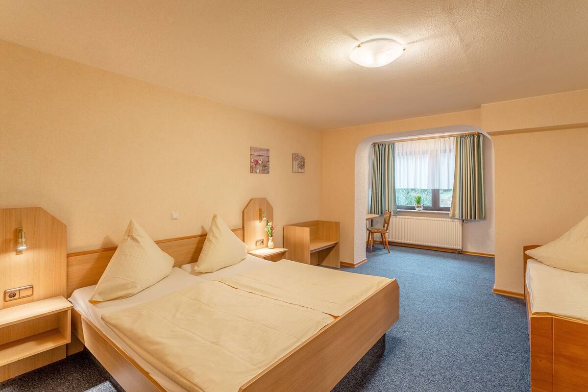 Una habitación de hotel con cama, mesitas de noche, escritorio y ventana con cortinas.