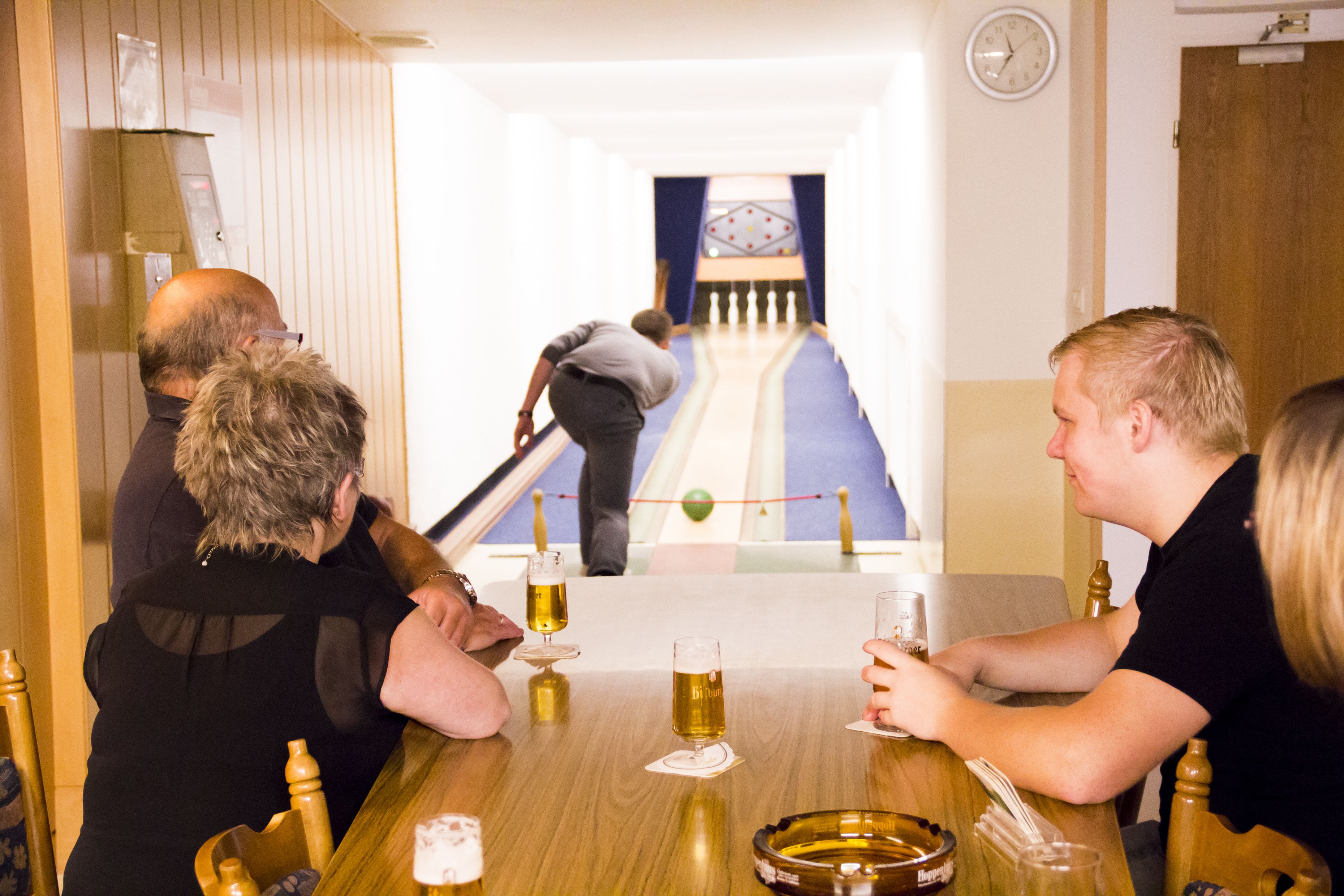 Eine Gruppe von Personen sitzt an einem Holztisch mit Biergläsern, einer Schüssel und einer Tablett.