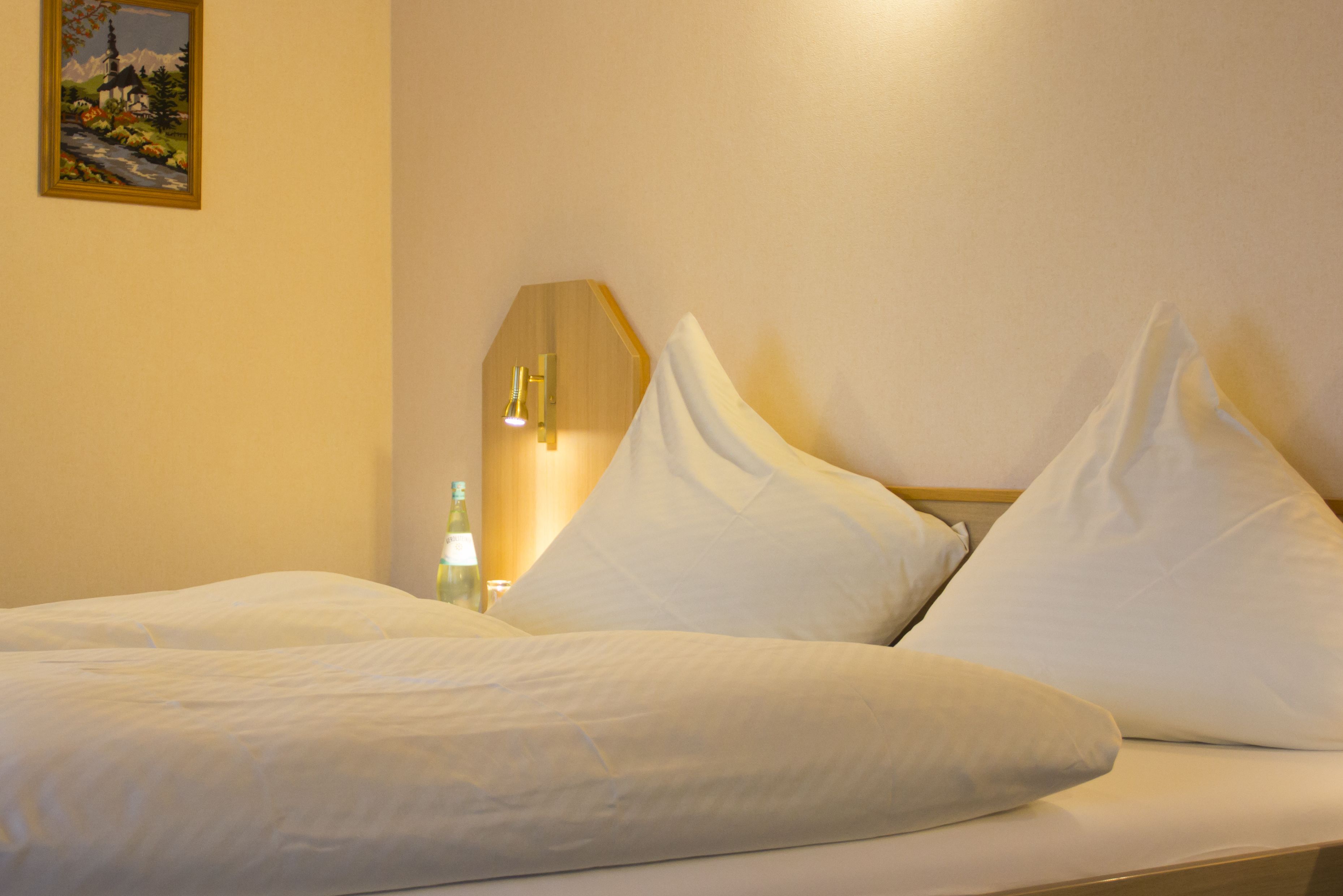 Ein Hotelzimmer mit einem ordentlich bezogenen Bett, einem wandmontierten Spiegel und einem gerahmten Bild.