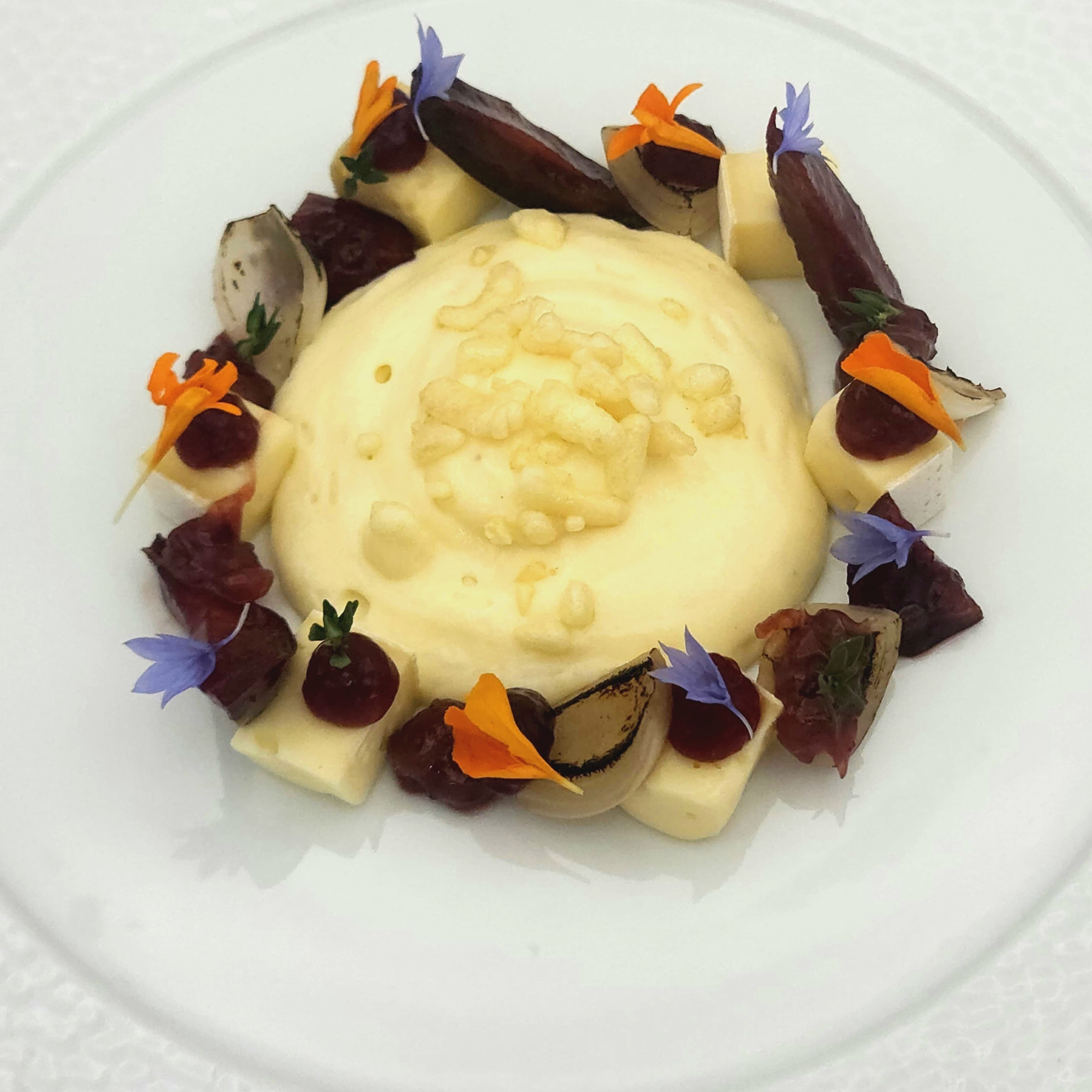 A dessert with a creamy center, surrounded by various fruits and garnishes on a white plate.