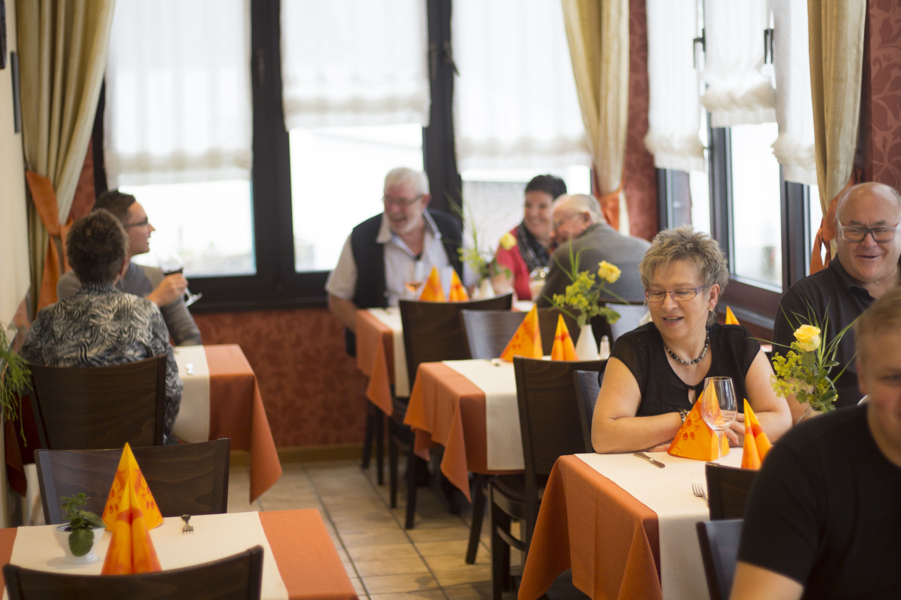 A restaurant with tables covered in orange tablecloths, chairs, and decorative orange napkins.