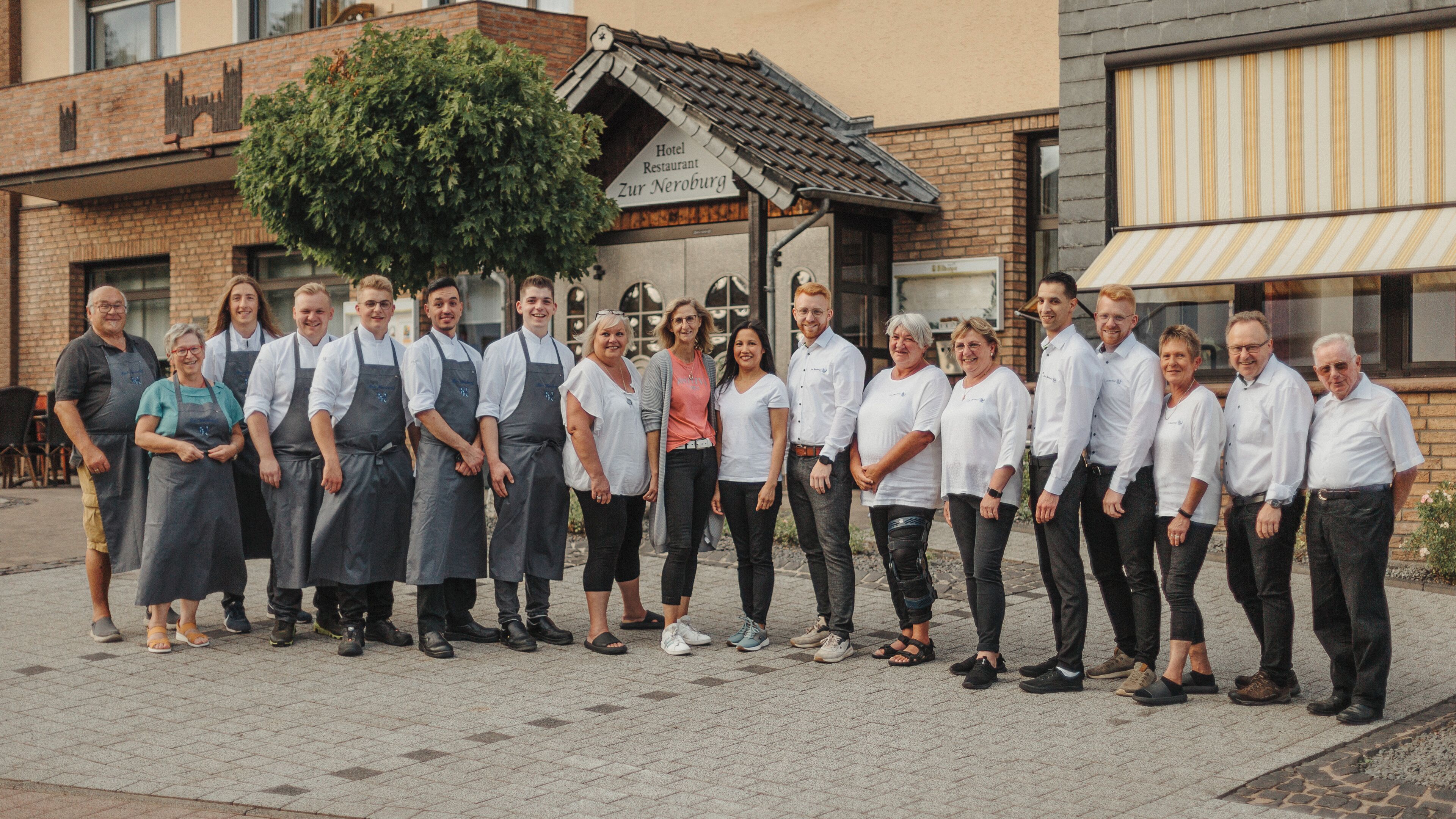 A group of people standing in front of a building with a sign that reads "Hotel Restaurant Zur Neuburg."