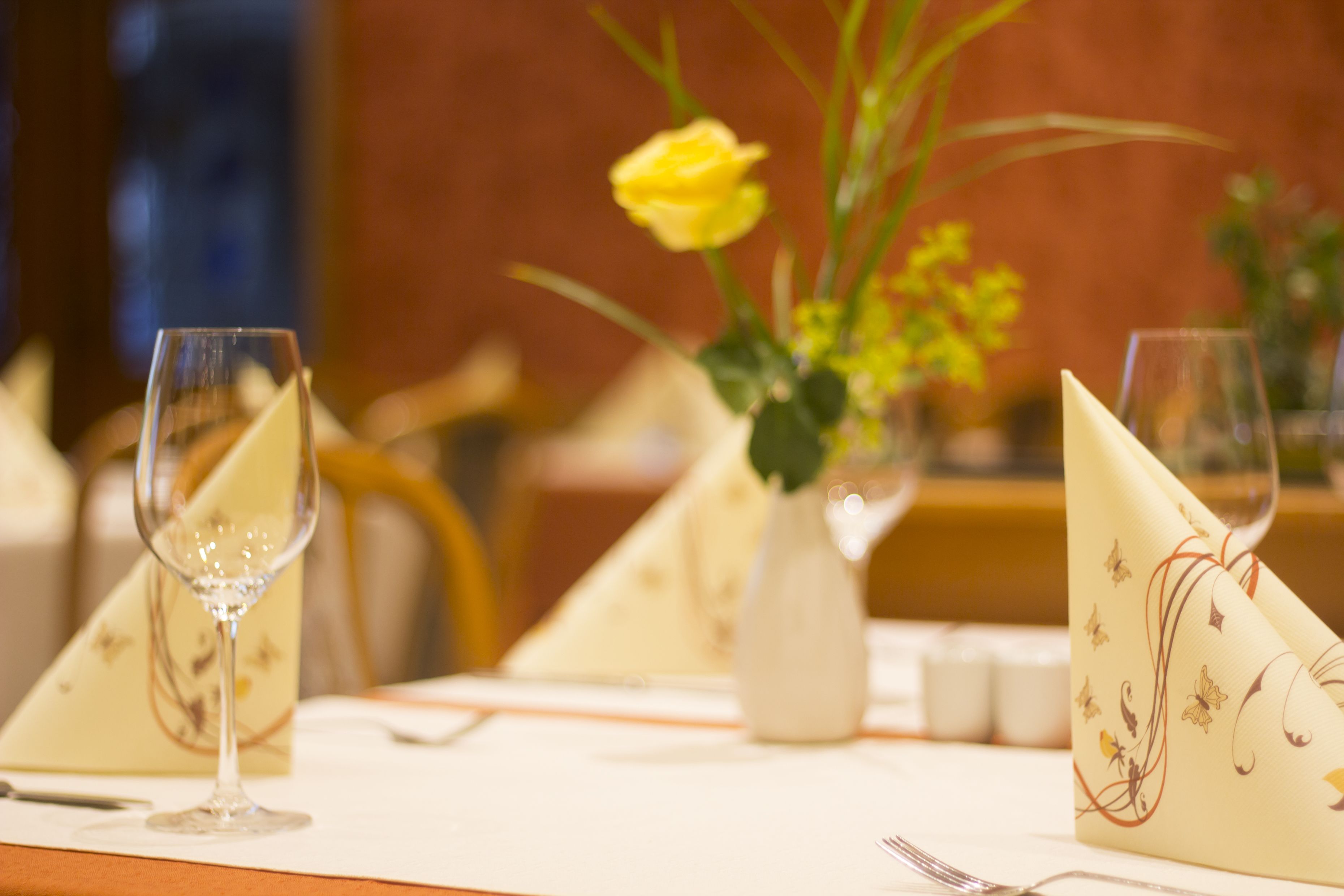 Una mesa de comedor con un florero de flores amarillas, una copa de vino y una servilleta doblada con diseño floral.