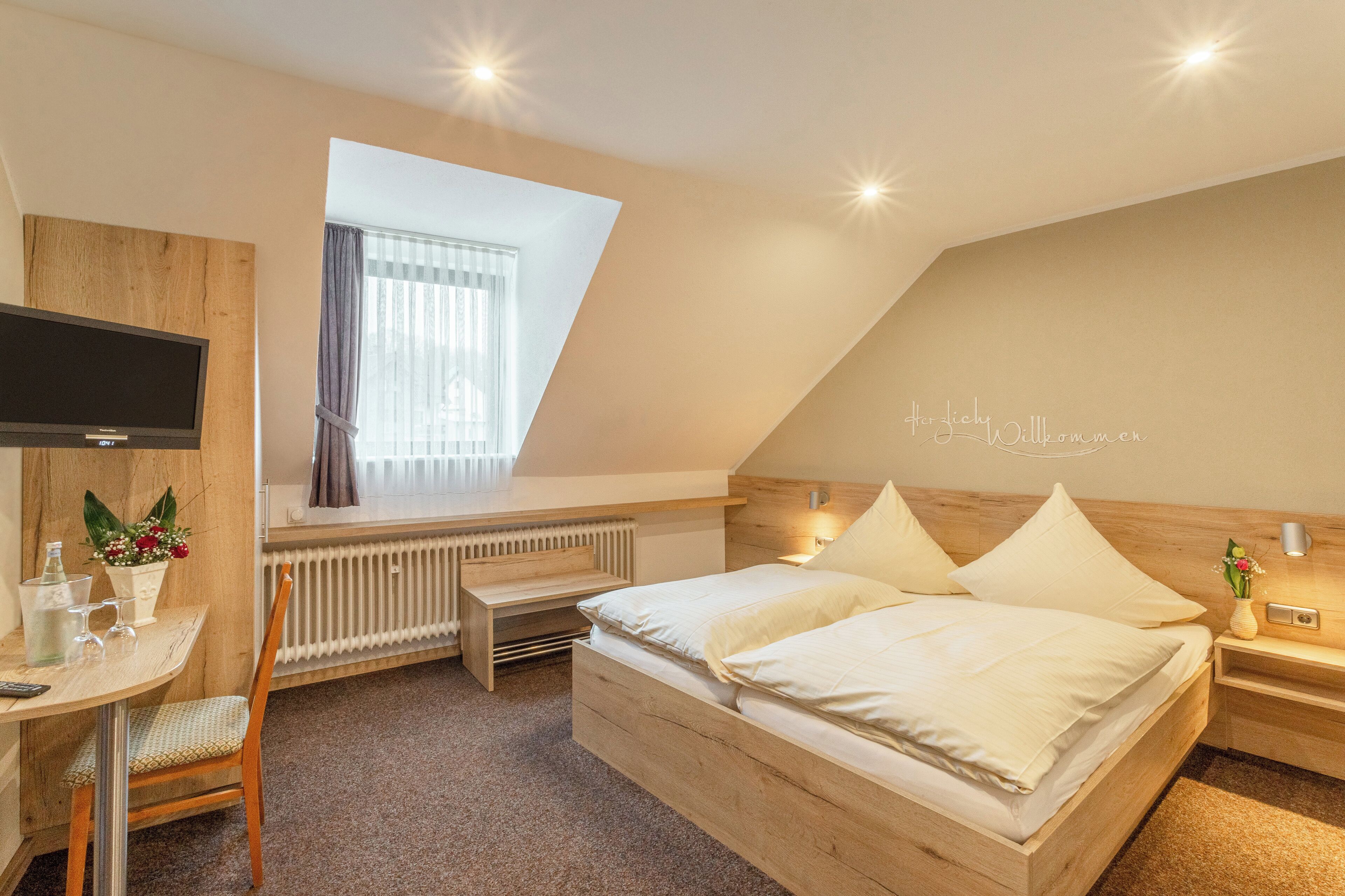 A bedroom with a bed, bedside table, lamp, and a TV.