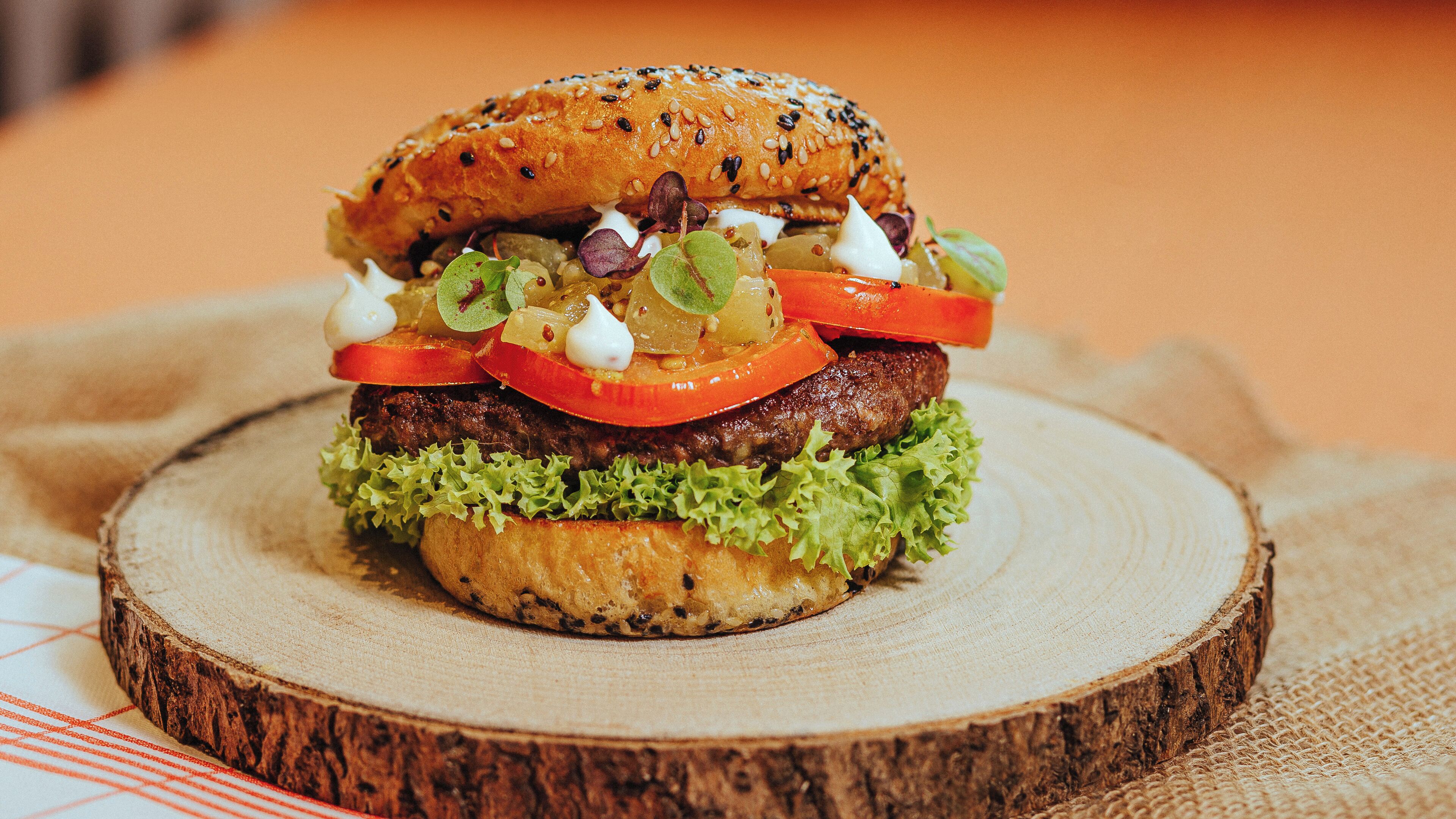 Un hamburger avec de la laitue, des tomates et un pain aux graines de sésame, présenté sur une planche en bois.