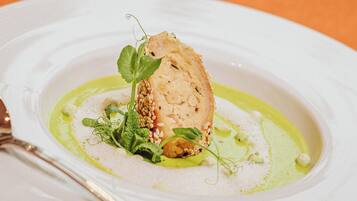 Un plato blanco con un bocado de comida decorado con hojas verdes y semillas de sésamo, acompañado de salsa verde.