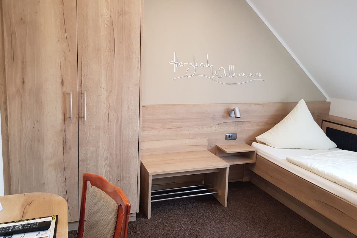 Un dormitorio con un armario de madera, un escritorio, una cama y una lámpara de pared.