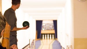 A bowling alley with a person holding a bowling ball, a bowling lane, and glasses of beer on the table. - Zur Neroburg (Neroth)