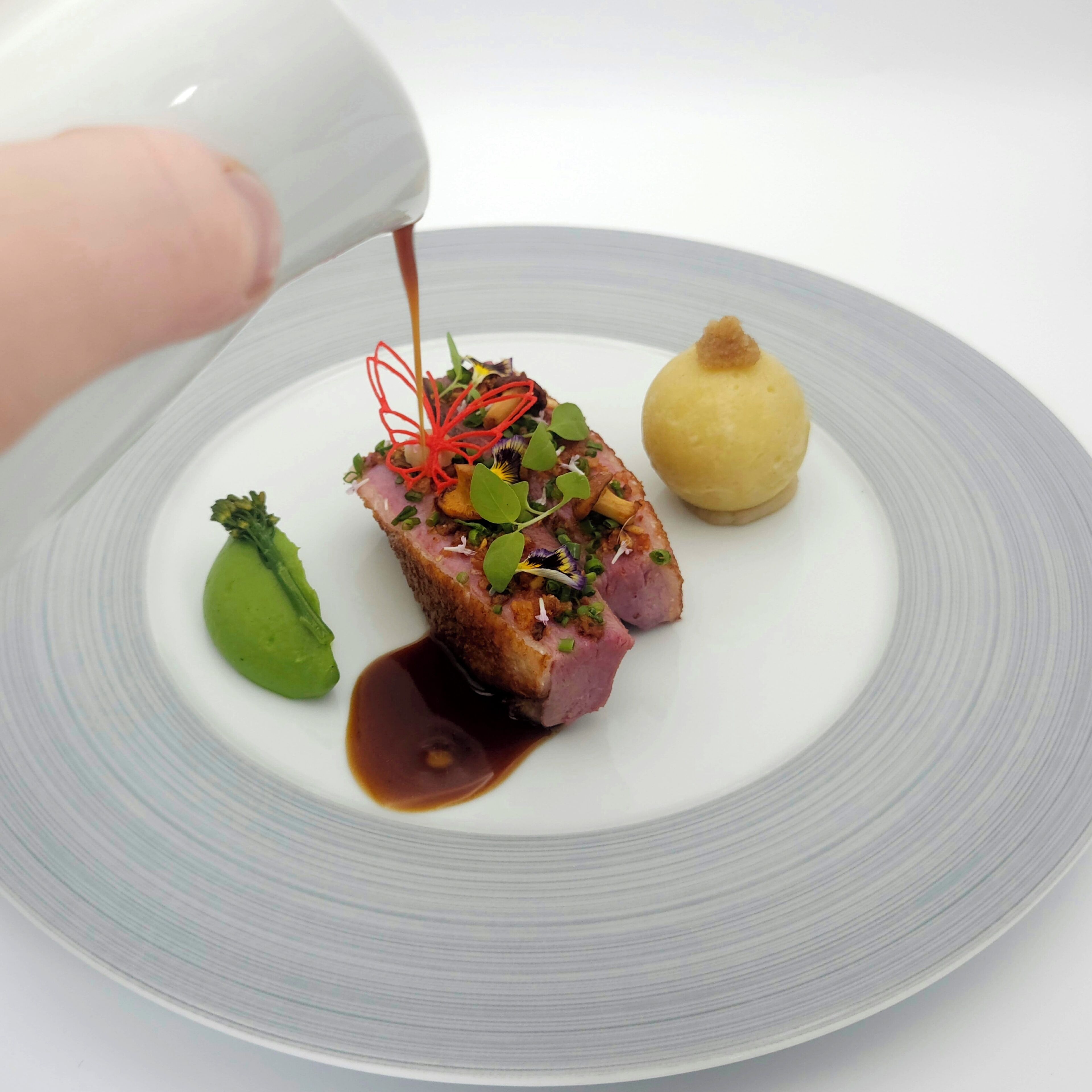 A plate with a piece of meat, a green leaf, and a yellow item.
