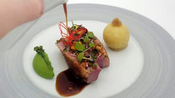 A plate with a piece of meat, a green leaf, and a yellow item.