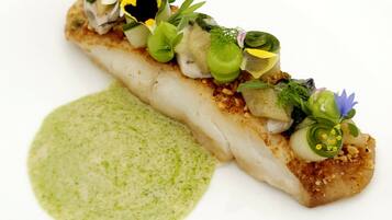 Un plato con salsa verde y un trozo de pescado cubierto de verduras y flores.