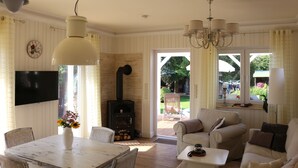 A living room with a fireplace, a dining table with a vase of flowers, and a television mounted on the wall. - Haus Elbromantik (Sandau)