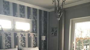 A bedroom with a large bed, striped wallpaper, a chandelier, and a window with a view of trees. - Haus Elbromantik (Sandau)