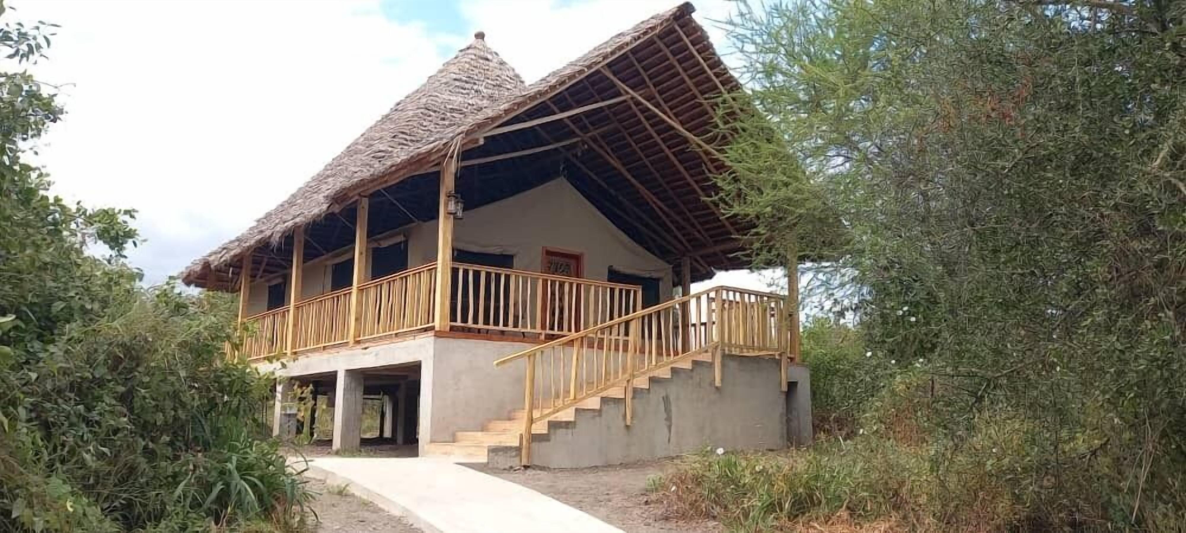 A two-story building with a thatched roof, a wooden balcony, and a concrete staircase leading to the entrance.