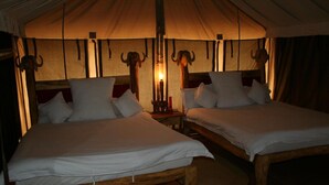 A tented accommodation with two wooden beds, each with white bedding and pillows, under a large tent with a central light source. - Roika Tarangire Tented Lodge (Tarangire National Park)