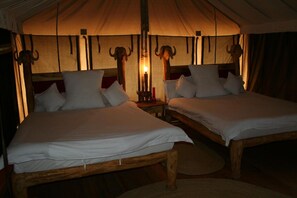 Alojamiento en carpa con dos camas de madera, cada una con ropa de cama y almohadas blancas, bajo una gran carpa con una fuente de luz central.