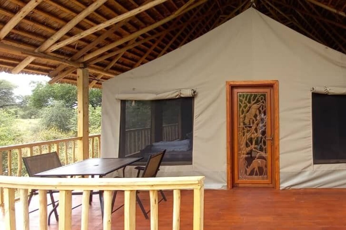 A tent with a wooden deck, a table, and chairs.