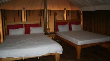 Um quarto em estilo tenda com duas camas de madeira, cada uma com roupa de cama branca e cabeceiras xadrez vermelhas.