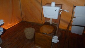 A compact, wooden-floored room with a simple toilet, a small woven basket, and a white refrigerator. - Roika Tarangire Tented Lodge (Tarangire National Park)