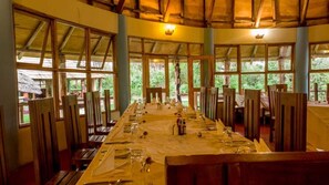 A long dining table set for a meal in a room with large windows and wooden beams. - Roika Tarangire Tented Lodge (Tarangire National Park)