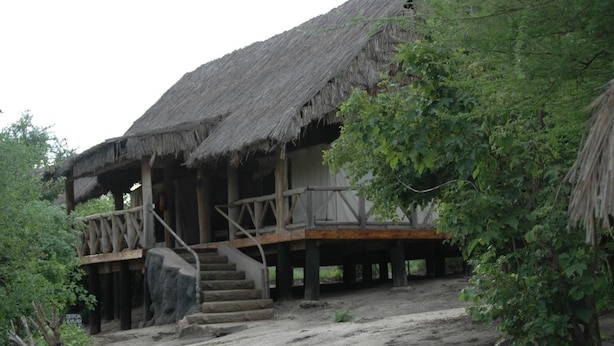 A rustic wooden structure with a thatched roof, a wooden staircase leading to a deck, and a sandy ground. - Roika Tarangire Tented Lodge (Tarangire National Park)