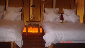 A room with two beds, a small wooden table, and a wall-mounted lamp. - Roika Tarangire Tented Lodge (Tarangire National Park)