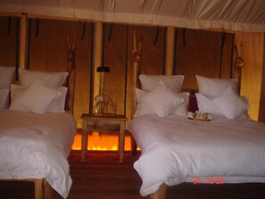 A room with two beds, a small wooden table, and a wall-mounted lamp.