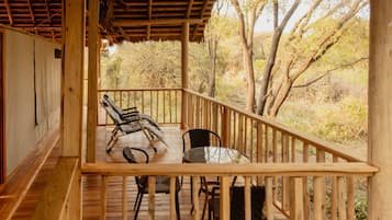 A wooden deck with a thatched roof, two lounge chairs, and a table.