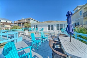 A deck with turquoise chairs and tables, a covered umbrella, and a view of the beach and ocean.