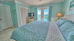 Un dormitorio con cama, ventilador de techo, televisor y balcón con vistas.
