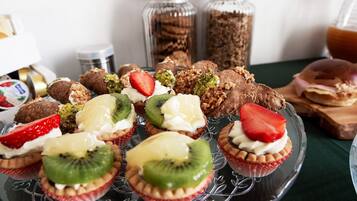 Variedad de postres, incluyendo cupcakes con frutas, pasteles y sándwiches sobre una mesa.