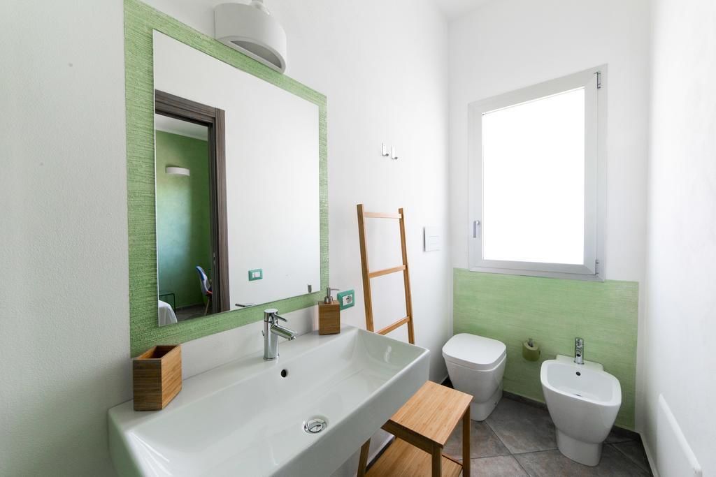 A bathroom with a large sink, a toilet, and a bidet. There is a mirror above the sink and a window on the wall.