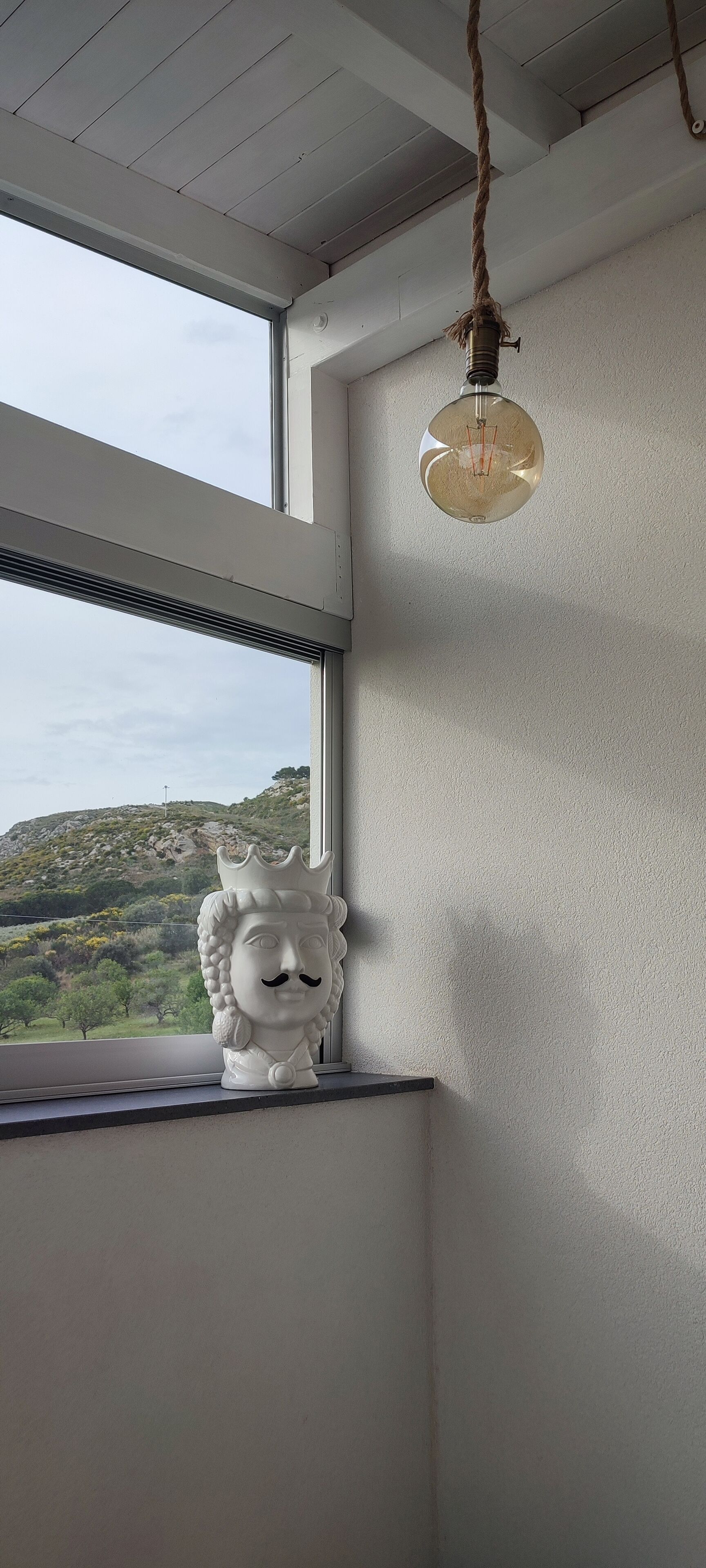 Una habitación con un ventanal grande, una lámpara colgante y una escultura decorativa de cabeza de león en el alféizar.