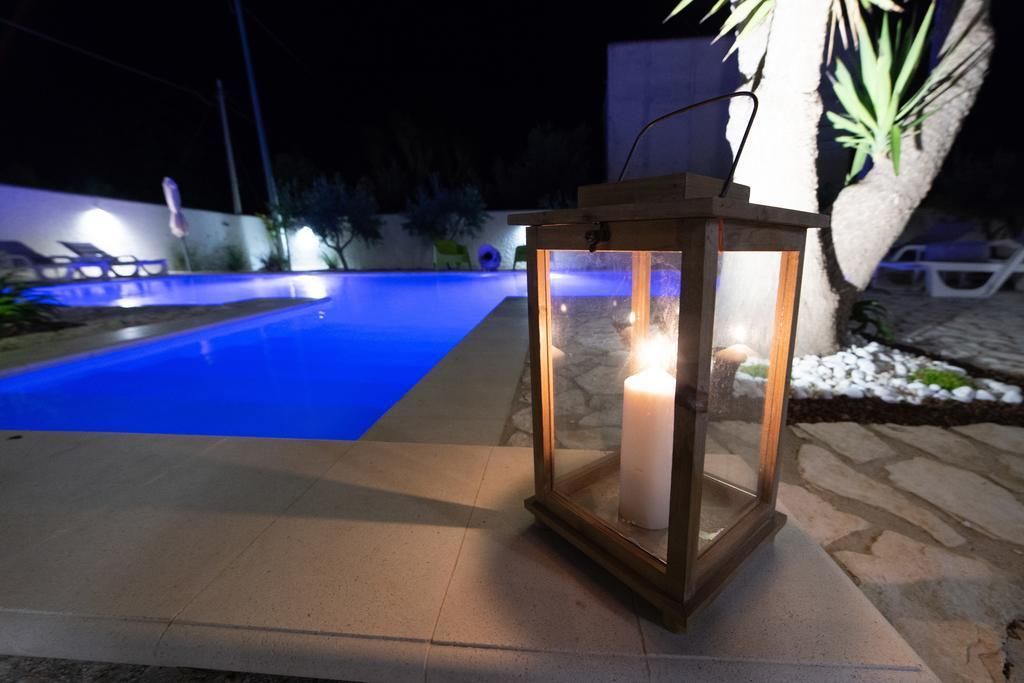 Una piscina con un tono azulado, un farolillo con vela y un sendero de piedra.