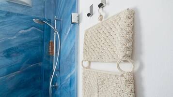 A bathroom with a blue marble shower enclosure, a white towel, and a white towel rack with hooks.