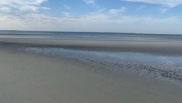 En strand med en bred sandstrand och milda vågor.