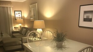 En matplats med ett vitt bord, fyra stolar och en krukväxt. I bakgrunden finns en soffa och en lampa.