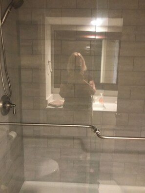 A bathroom with a glass shower enclosure, a visible toilet, and a mirror reflecting a person.