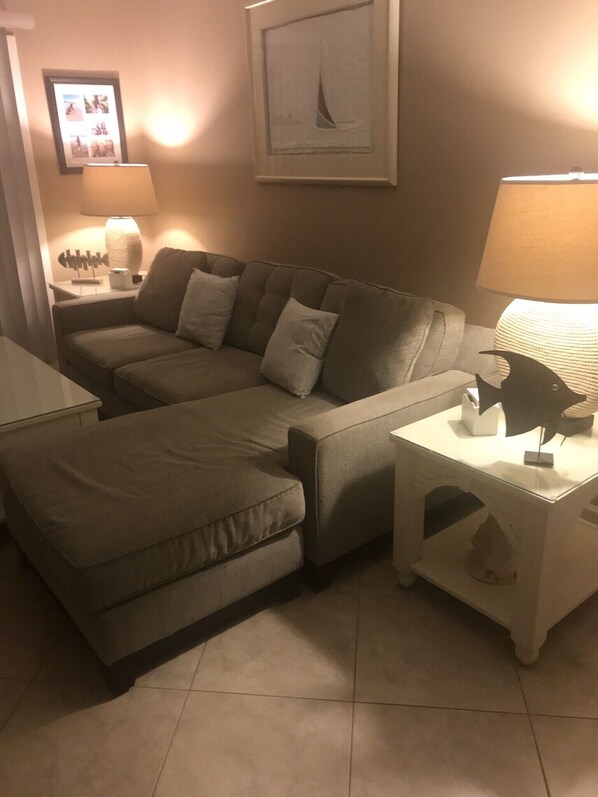 A living room with a sectional sofa, a small table with a lamp, and a framed picture on the wall. - Beautiful, Easy Ocean Access (Hilton Head)