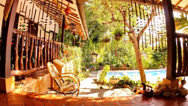 Un espacio al aire libre cubierto con una silla de madera, una piscina y plantas colgantes.