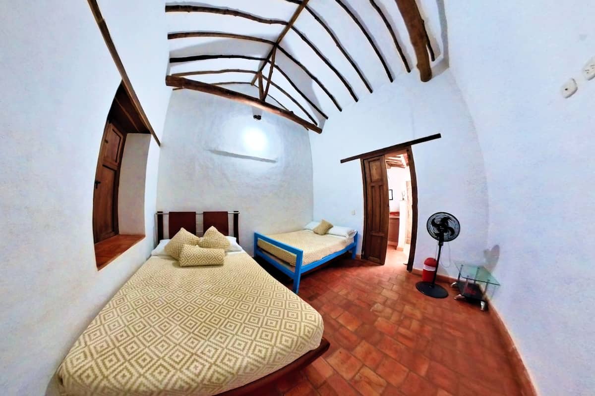 A compact bedroom with a bed, a small seating area, and a fan.
