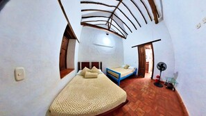 A compact bedroom with a bed, a small seating area, and a fan. - Hostal Santa Mónica (Barichara)