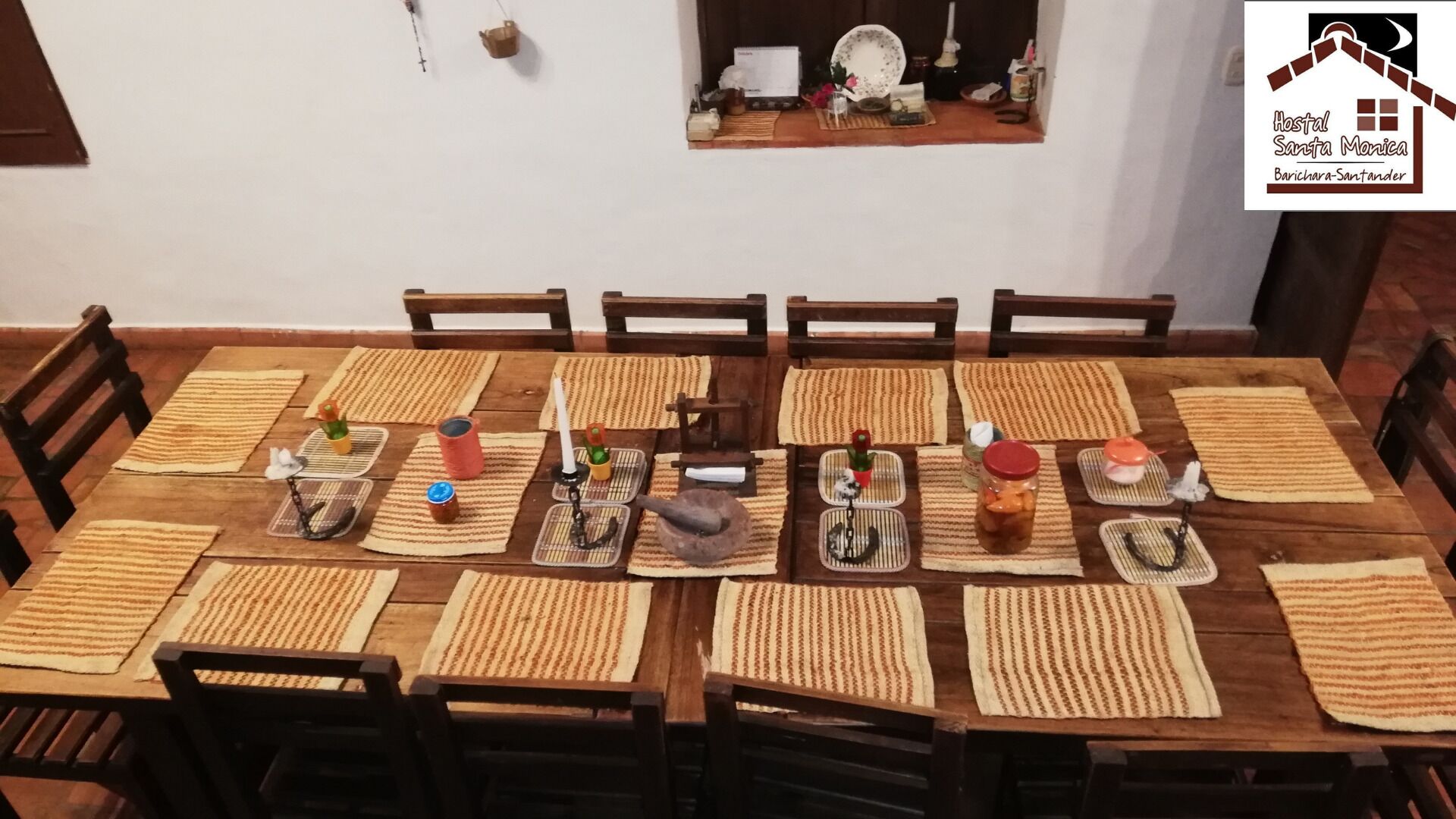 Una mesa de comedor lista, con manteles individuales, sillas y diferentes alimentos.