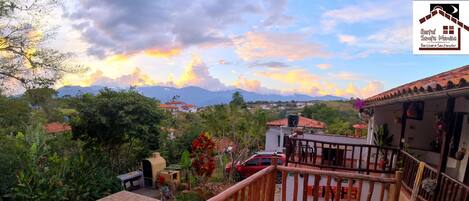 Relax on the stone patio, surrounded by lush trees and a distant mountain range, with access to a swimming pool and a balcony with a railing.