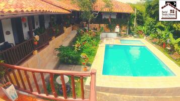 Uma área de piscina com um deck ladrilhado, uma cerca de madeira e uma placa para Hostal Santa Monica ao fundo.