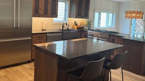 A modern kitchen with dark wood cabinets, stainless steel appliances, and a large island with bar stools. - Lakefront resort, pool, tennis, pickleball with a private beach, fast EV charger (Whitefish)
