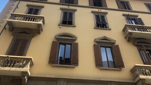 A multi-story building with a yellow facade, multiple windows with shutters, and balconies with railings. - Fortezza Fourth Floor - 6 pax (Florence)