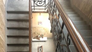 A staircase with a metal railing and a wooden handrail, leading to a landing with a bench and a wall-mounted light fixture. - Fortezza Fourth Floor - 6 pax (Florence)
