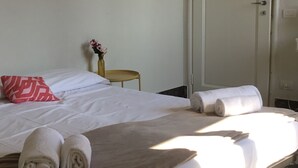 A neatly made bed with white linens, a red patterned pillow, and rolled towels. - Fortezza Fourth Floor - 6 pax (Florence)